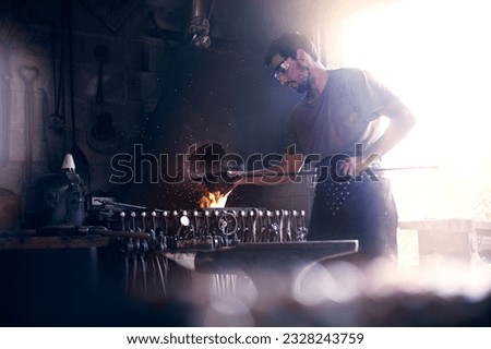 Image, Stock Photo Focused young blacksmith heating and striking metal on anvil in workshop
