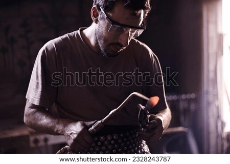 Similar – Image, Stock Photo Focused young blacksmith heating and striking metal on anvil in workshop