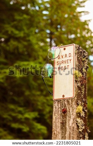Pair of eyeglasses hanging on the side of a pole with the sign G.V.R.D survey post in front of forest trees Stock fotó © 