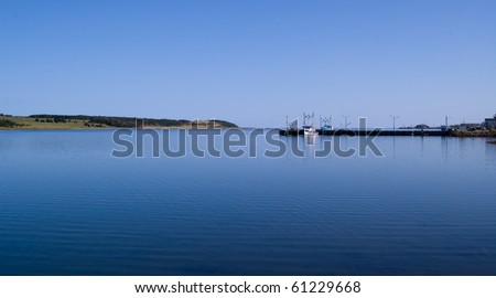 Boats moored at the docks on calm ocean waters in early morning light; Cape Breton, NS, Canada