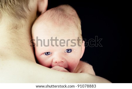 New Born Baby with Bright Blue Eyes Looking Over Father\'s Shoulder - Isolated over Black