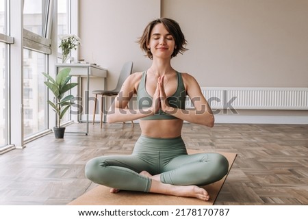 Beautiful cute sporty woman doing exercise in bright room. Focused on brunette sitting on the floor practicing yoga wear tip and leggings. Home mood, lifestyle  Foto d'archivio © 