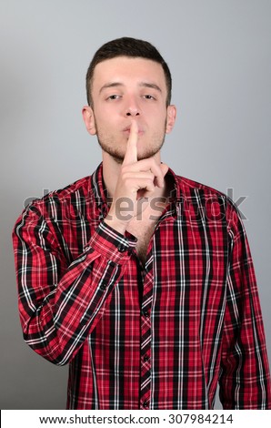 Businessman pointing finger over lips, asking for silence  over gray background. Looking at camera