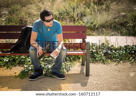 Guy sitting on a park bench  with a bottle of wine