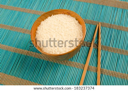 A bowl with raw rice and chopsticks on a bamboo mat