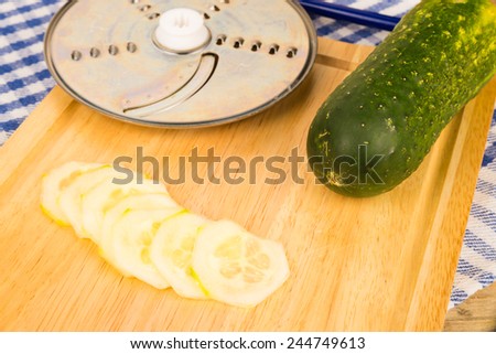 Cucumber slices next to a food processor slicing disk
