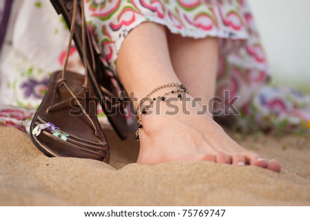 Female feet and leather sandals on a sandy dune in spring