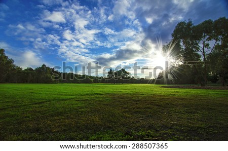 Beautiful outdoor open space park with blue sky and morning sun. Green grass and cloudy day.