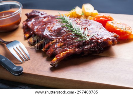 Pork Spareribs with tomato and fried potatoes on wooden plate served with BBQ sauce