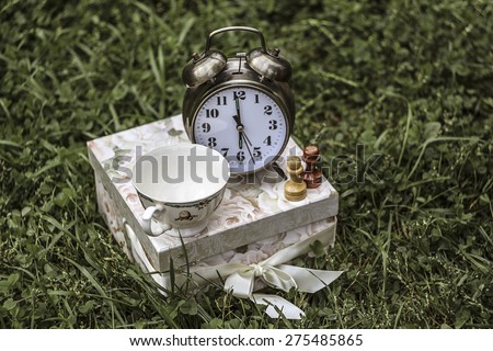 6 o\'clock - tea time. An alarm clock, a tea cup and two pawns on a present box.