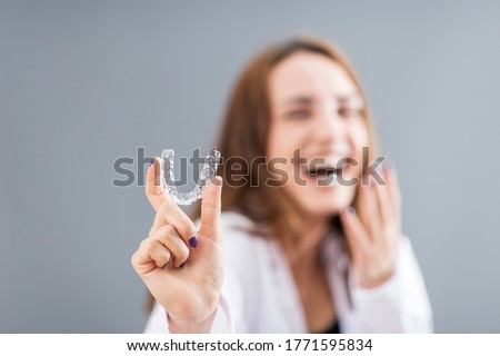 Beautiful smiling Turkish woman is holding an invisalign bracer in a studio with grey background