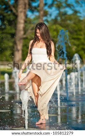 young beautiful caucasian brunette girl playing at an outdoor water fountain .Sunny day