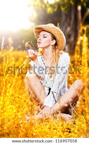 fashion portrait woman with hat and white shirt sitting on a hay stack.very cute blond woman sitting down outdoor on the yellowgrass with a hat