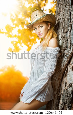 fashion portrait woman with hat and white shirt sitting on a hay stack.very cute blond woman sitting down outdoor on the yellow grass with a hat