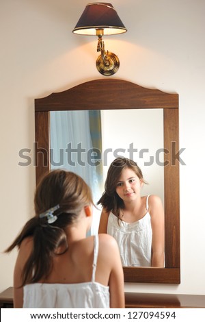A beautiful teen girl studies her appearance as she looks into the mirror at her beautiful young reflection. Teen girl happy with their appearance in the mirror