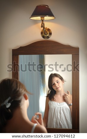 A beautiful teen girl studies her appearance as she looks into the mirror at her beautiful young reflection. Teen girl happy with their appearance in the mirror