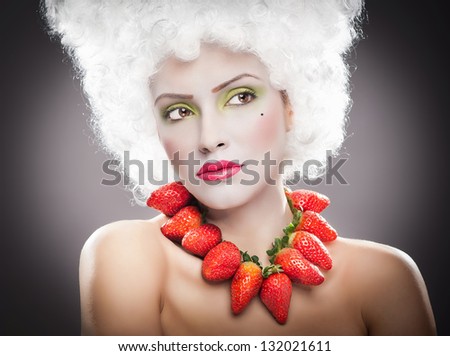 Creative makeup beauty shot of model with strawberries, artistic edit .Woman with strawberry necklace, wig and makeup professionally posing in studio.Beauty with strawberry.
