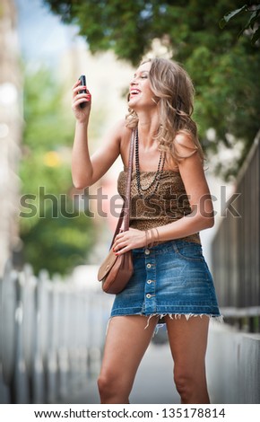 fashion blonde girl with short skirt at playing with mobile phone.Young attractive woman talking on a cell phone in a  street.happy young woman play by mobile phone on the street