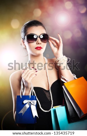 Woman with glasses  holding shopping bags against a black background.Style beauty girl with shopping bags.Portrait of stunning young woman in sunglasses carrying multicolored shopping bags .