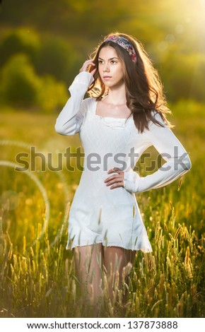 Girl with white shirt on the field at sunset.Young beautiful woman standing in wheat field .Vintage looking picture of a Young  woman standing in a wheat field .Sun at early sunset in the background.