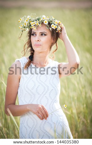 Young girl with wreath on golden wheat field.Portrait of beautiful blonde girl with wreath of wild flowers.Beautiful woman enjoying daisy field, pretty girl relaxing outdoor, harmony concept