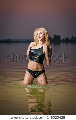 Attractive blonde woman in water at sunset .Beautiful swimsuit model.The beautiful sensual bikini model posing against a setting sun on a body of water .Erotic art photo