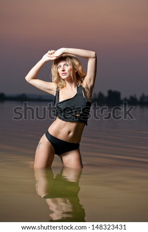 Attractive blonde woman in water at sunset .Beautiful swimsuit model.The beautiful sensual bikini model posing against a setting sun on a body of water .Erotic art photo