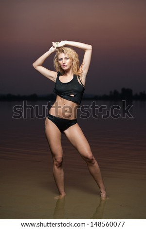 Sexy blonde woman in water at sunset .Beautiful swimsuit model.The beautiful sensual bikini model posing against a setting sun on a body of water .Erotic art photo