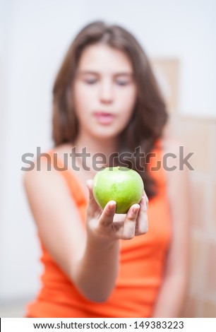 teen Girl holding a beautiful, fresh green apple indoor, selective focus on apple.Pretty teen girl concentrated  hold green fresh apple in hand.. girl holding an green apple, healthy eating