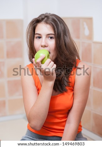Pretty teen girl eating apple, indoor.Beautiful teenage girl biting an apple .Picture of beautiful teenage biting a green apple