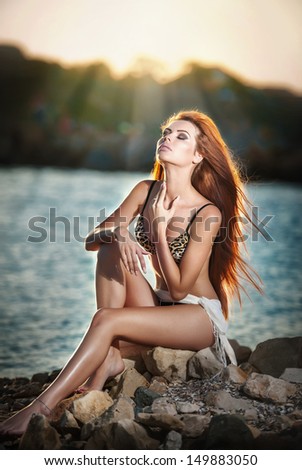 beautiful woman with veil in a bathing suit standing on the beach at sunset.Portrait of a beautiful woman in bikini on the beach.Tan beautiful red hair woman posing on sea beach on warm background