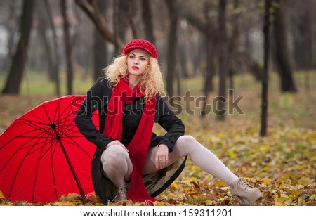 Attractive young woman in a autumn fashion shoot. Beautiful fashionable young girl with red umbrella, red cap and red scarf in the park