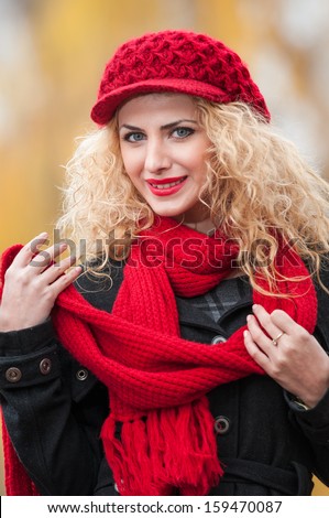 Attractive young woman in a autumn fashion shoot. Beautiful fashionable young girl with red cap and red scarf in the park. Blonde women with red accessories posing outdoor. Nice fair hair girl