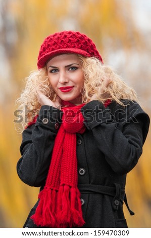 Attractive young woman in a autumn fashion shoot. Beautiful fashionable young girl with red cap and red scarf in the park. Blonde women with red accessories posing outdoor. Nice fair hair girl