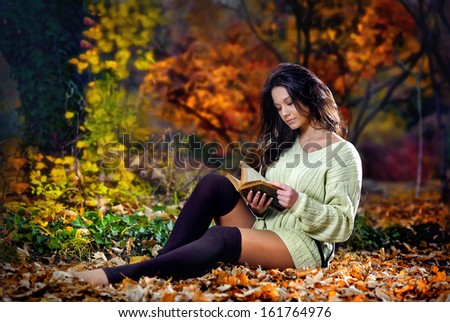 Young caucasian sensual woman reading a book in a romantic autumn scenery.Portrait of pretty young girl in the forest in autumn day.Fashion portrait of a beautiful young woman in autumn forest