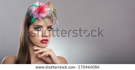 Hairstyle and Make up - beautiful genuine natural brunette with colored flowers in her long hair. Art portrait of an attractive woman with beautiful eyes and flowers in her hair on grey background