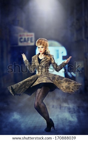 Attractive elegant blonde young woman wearing an outfit with Russian influence in urban fashion shot. Beautiful fashionable young girl with long legs and fur cap posing spinning on street
