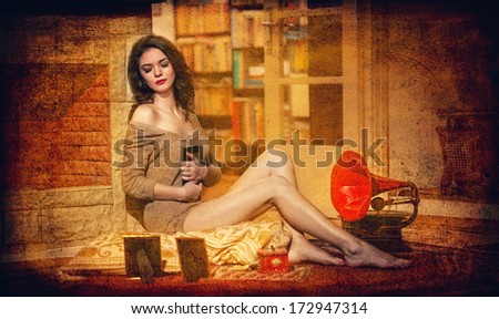 Beautiful sexy woman near a red gramophone surrounded by photo frames in vintage scenery. Portrait of girl in slim fit short dress posing comfortable in cosy scenery. Attractive brunette female.