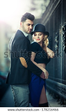 Couple in love in railway station. Beautiful well-dressed couple standing on railway platform. Handsome brunette young man holding a fashionable blonde with hat next to a train