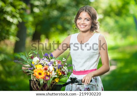 Beautiful girl wearing a nice white dress having fun in park with bicycle. Healthy outdoor lifestyle concept. Vintage scenery. Pretty blonde girl with retro look with bike and basket with flowers
