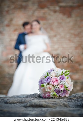 Newly-married couple and wedding bouquet in the foreground. Wedding bouquet with the wedding couple in the background