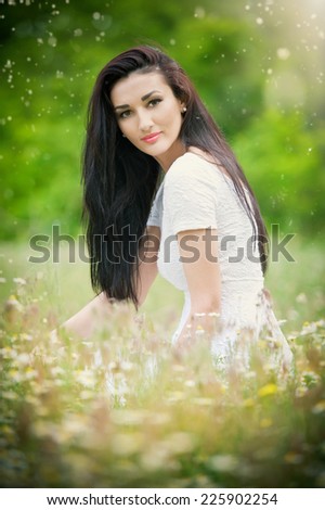 Beautiful young woman in wild flowers field.Portrait of attractive brunette girl with long hair relaxing in nature, outdoor shot in sunny day. Lady in white enjoying daisy field, harmony concept