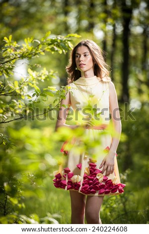Young beautiful girl in a yellow dress in the woods. Portrait of romantic woman in fairy forest.  Stunning fashionable teenage model in summer meadow, outdoor shot. Cute brunette long hair female.
