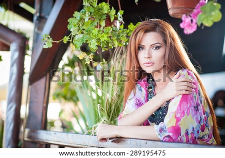Beautiful female portrait with long red hair outdoor. Genuine natural redhead with bright colored blouse in park. Portrait of a attractive woman with beautiful eyes daydreaming, outdoor shot