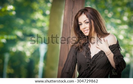 Beautiful female portrait with long brown hair outdoor. Genuine natural brunette with gorgeous eyes posing in park. Portrait of a attractive woman with black dress sitting on a wooden pavilion