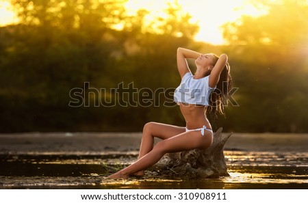 Sexy brunette in white swimsuit posing in river water. Young female in lake during sunset. Perfect body girl posing provocatively in summer evening at beach. Sensual attractive long hair woman
