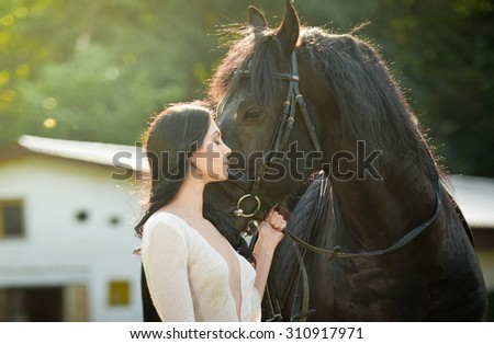 Fashionable lady with white bridal dress near brown horse. Beautiful young woman in a long dress posing with a friendly black horse. Attractive elegant female with horse, close-up photo
