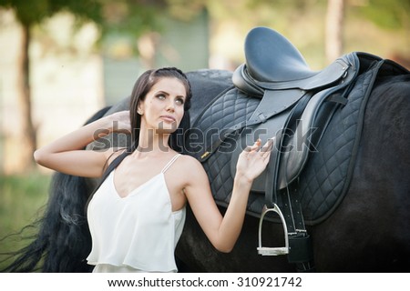 Fashionable lady with white bridal dress near brown horse in nature. Beautiful young woman in a long dress posing with a friendly black horse. Attractive elegant female with horse, sunny summer day