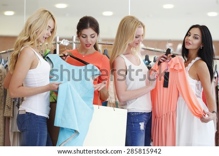 Young happy women choosing dress on sale in shopping mall
