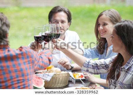Friends clink glasses of red wine at outdoor dinner